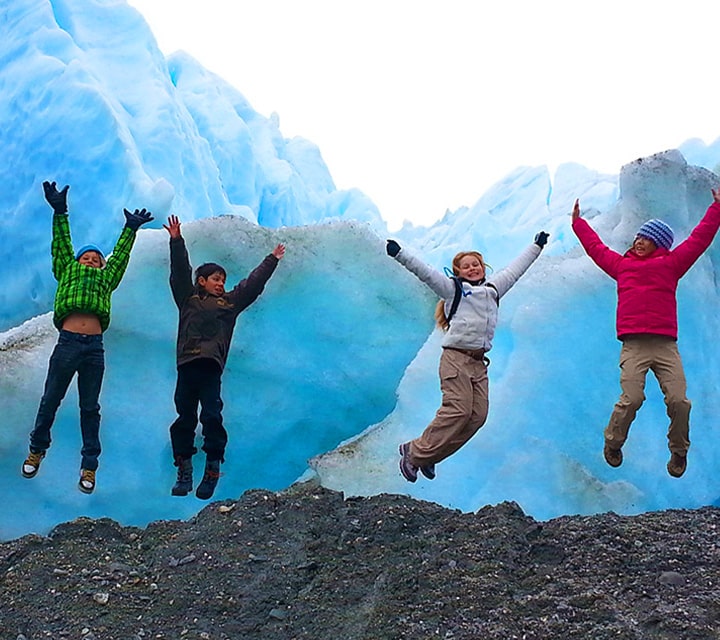 Young kids jumping with glee next to a glacier in Patagonia